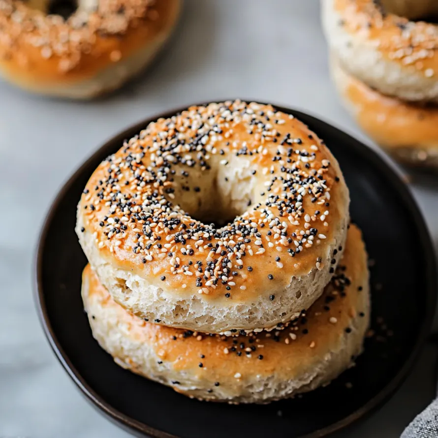 A plate stacked with bagels sprinkled with sesame seeds.