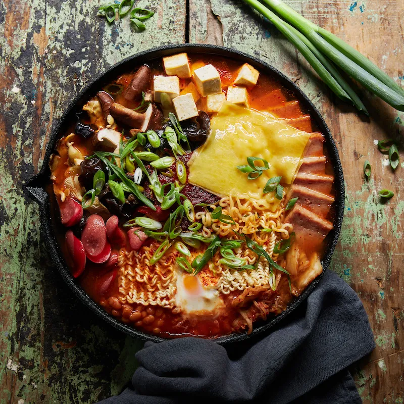 A hearty bowl with meat, noodles, and fresh veggies—fork and knife resting nearby.